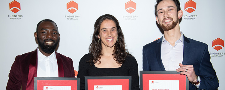 three people stand with framed awards