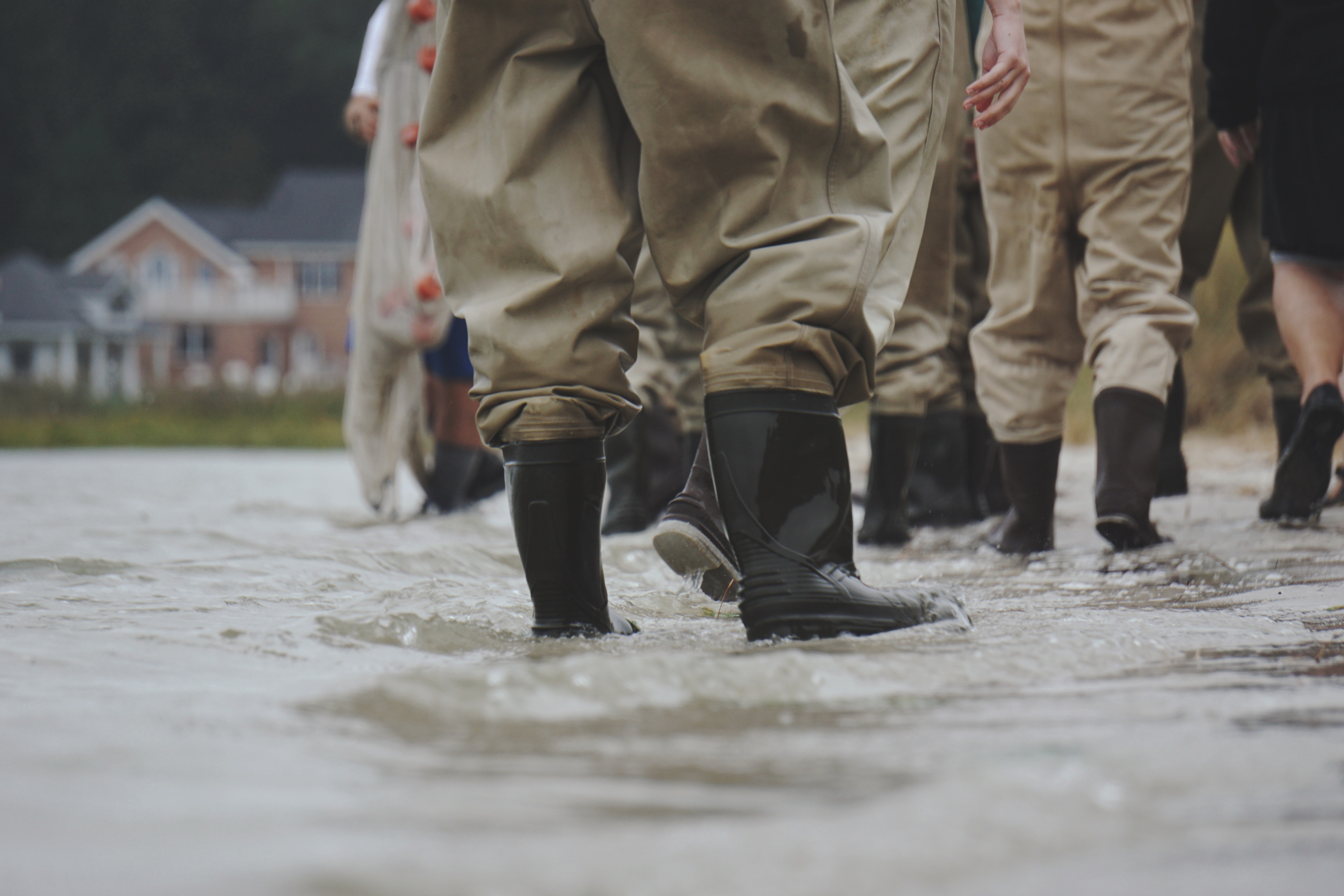 Close up on a group of people walking through grey water with black gumboots on
