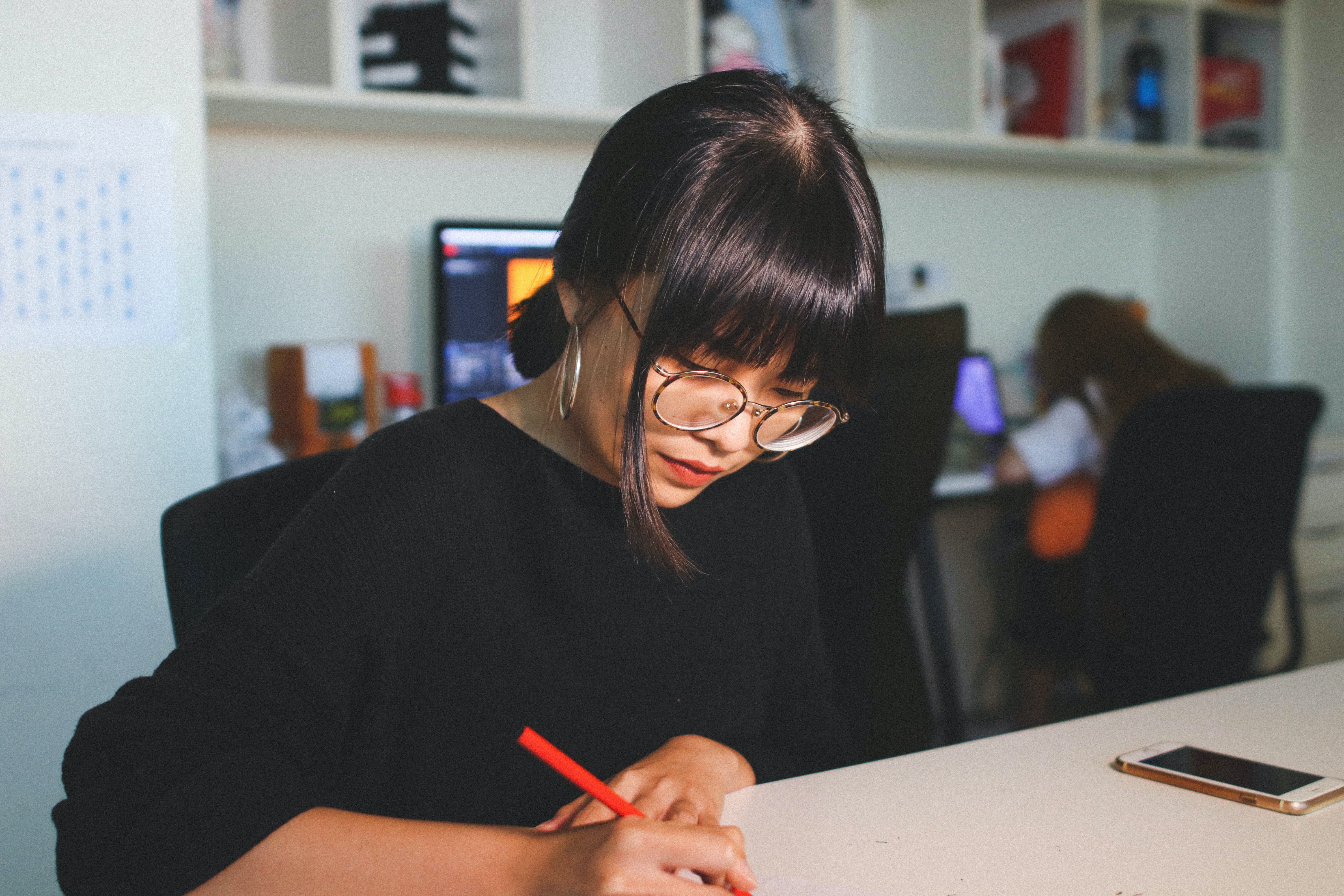 woman with glasses using a red pen to write on paper at a desk