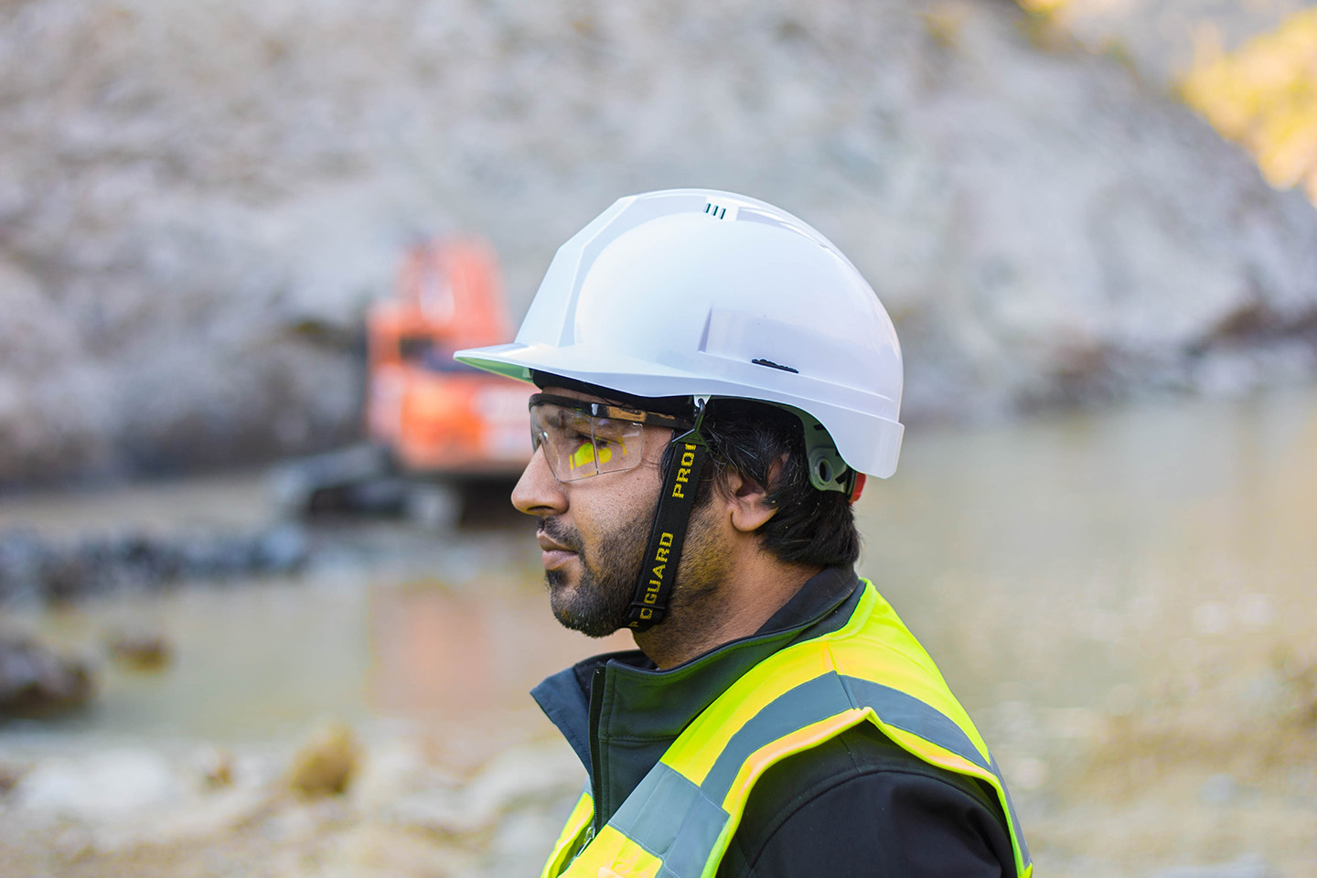 Man with yellow safety vest and white safety helmet standing in front of a small body of water