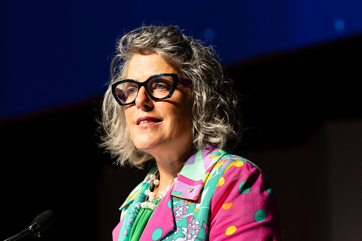Romilly Madew speaking at a conference, close up shot, wearing a pink and green patterned blazer