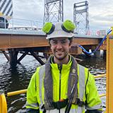 Jarrod with safety gear on standing on a wharf in front of the sea